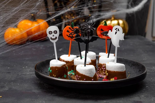 Dolce Halloween, marshmallow ricoperti di cioccolato con zucchero e decorazioni di Halloween su un piatto nero, foto con messa a fuoco morbida — Foto Stock