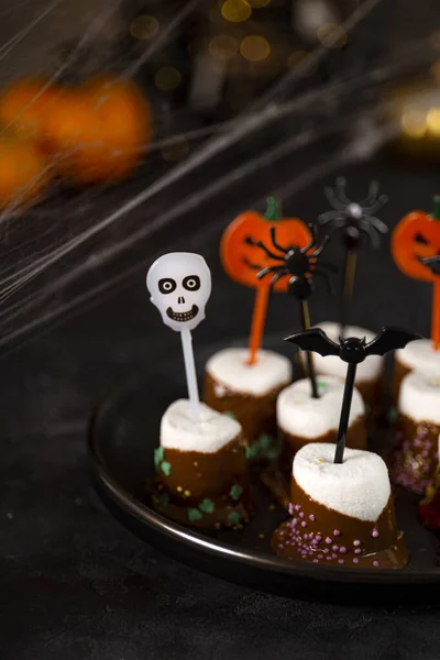 Dolce Halloween, marshmallow ricoperti di cioccolato con zucchero e decorazioni di Halloween su un piatto nero, foto verticale con messa a fuoco morbida — Foto Stock