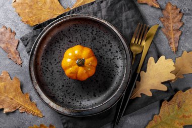  Sonbahar masa düzenleme konsepti. Tabak, altın çatal bıçak, balkabağı ve sonbahar yaprakları gri arka plan manzaralı