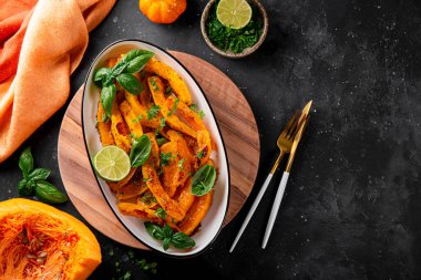 Beyaz oval tabakta fesleğenli ve otlu fırınlanmış balkabağı ve koyu gri arka plan görüntüsü, metin için boşluk kopyala. Sonbahar Sebze Tabakları