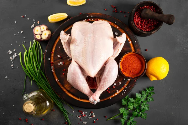Ahşap kesim tahtasının üzerinde çiğ tavuk ve onu pişirmek için baharatlar, yazı için bedava alan. Koyu gri arka plan. Yüksek kalite fotoğraf