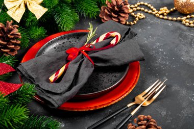 Noel masası konseptini bir şenlik masasına yakın konsept haline getiriyor. Tabak, peçete, baston şekeri, altın çatal bıçak takımı ve gri arka planda noel süslemeleri.