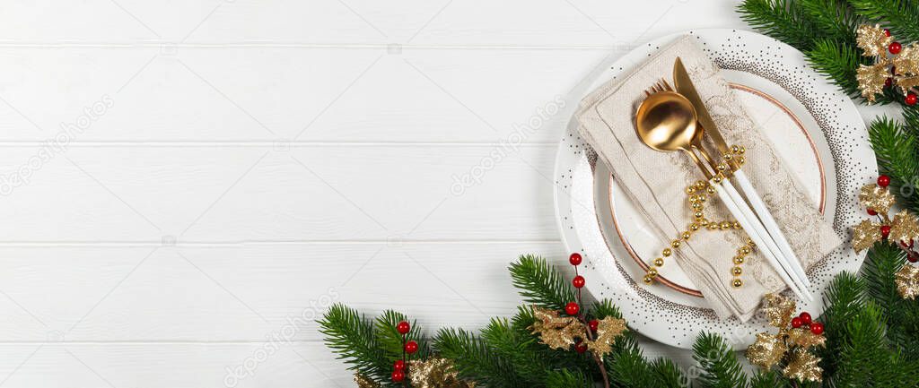 Web banner Christmas table setting concept on white wooden background. Plate, napkin and golden cutlery and christmas decorations on white background top view, free space for text. High quality photo