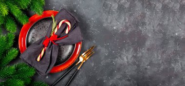 Web afişi, koyu gri arka planda Noel masası konsepti. Tabak, peçete, şeker kamışı, altın çatal bıçak takımı ve gri arka planda Noel süslemeleri, metin için boş alan