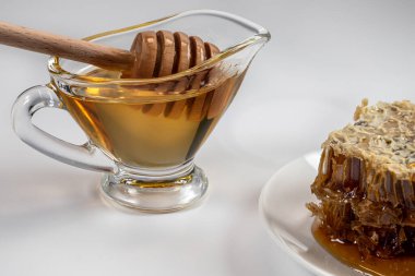 Taze sıvı bal, beyaz arka planda cam bir kapta bal çubuğu. Taraktaki bal.