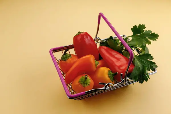 Detailní záběr nákupního vozíku na žlutém pozadí. Sladká paprika žlutá červená, petržel. — Stock fotografie