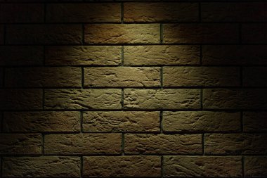Yukarıdan parlak ışıklandırmalı sarı-kırmızı tuğla duvar. Tuğla dokusu. Koyu tuğla arkaplan.