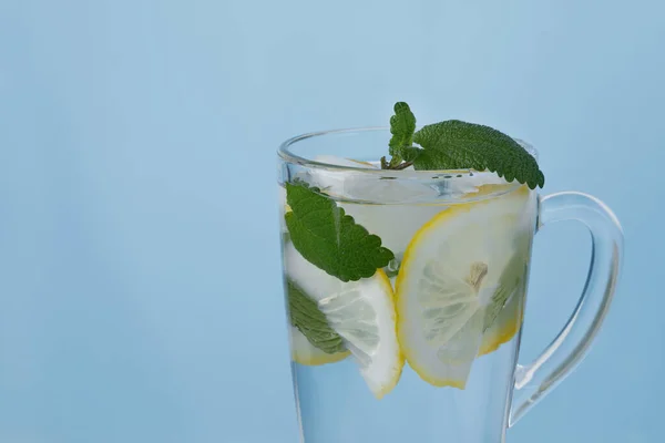 Buz küpleri, limon dilimleri ve mavi arka planda cam bir fincanda nane yaprakları..