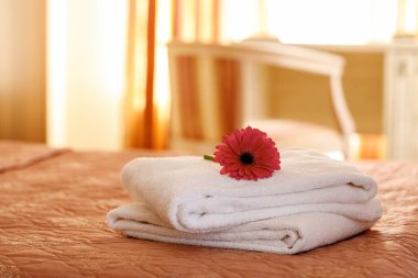 Otel odasındaki yatağın üzerinde çiçek olan temiz beyaz havlular..