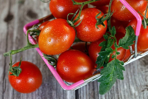 Nákupní košík plný cherry rajčat na dřevěném pozadí. — Stock fotografie