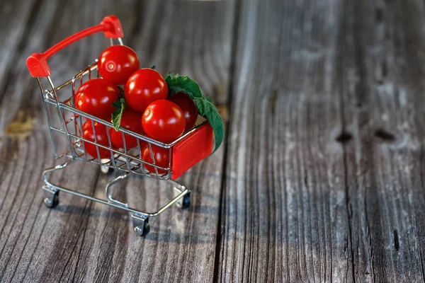 Nákupní košík plný cherry rajčat na dřevěném pozadí. — Stock fotografie