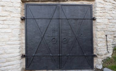 Taş bir binanın, eski bir kalenin, beyaz bir taş duvarın karşısında, demir siyah, ağır kilitli kapısı..