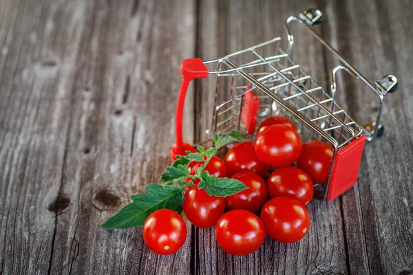 Padlý nákupní košík s cherry rajčaty na dřevěném pozadí. — Stock fotografie