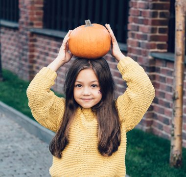 Cadılar Bayramı için turuncu kazaklı, balkabaklı ve siyah tuğlalı komik kız çocuğu. Cadılar bayramı için turuncu kazaklı ve siyah kotlu gülen kız çocuğu.