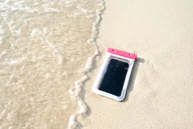Akıllı telefondan su geçirmez çanta, su altında fotoğraf çekmek için telefon. Su geçirmez kasadaki telefon su altında, kumların üzerinde..