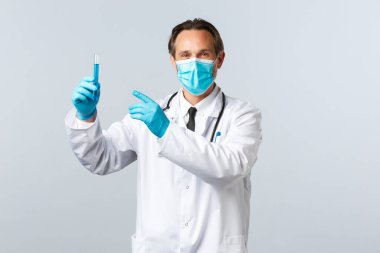 Covid-19, virüsü önleme, sağlık çalışanları ve aşı konsepti. Tıbbi maskeli ve eldivenli tatmin olmuş gülümseyen doktor test tüpünü aşı numunesiyle işaret ediyor, ilacı onaylıyor.