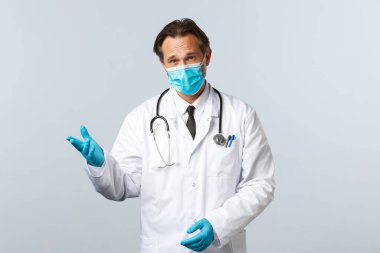 Covid-19, virüsü önleme, sağlık çalışanları ve aşı konsepti. Tıbbi maskeli ve eldivenli ciddi görünümlü bir doktor hastalarla konuşuyor, koronavirüs salgını sırasında alınan önlemleri açıklıyor.