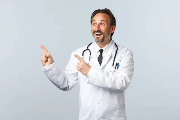 Covid-19, coronavirus outbreak, 의료 종사자와 전염병 컨셉트. 왼쪽 상단의 손가락을 가리키는 하얀 가운을 입고 행복 한 미소를 짓고 있는 남성 의사 약물이나 클리닉 현수막을 보여 주면서 즐겁게 웃고 있다 — 스톡 사진