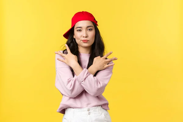 Persone emozioni, stile di vita tempo libero e concetto di bellezza. Fresco e impertinente elegante ragazza asiatica in rosso hip hop cap, mostrando gesto swag e sorridere audace, in piedi fiducioso su sfondo giallo — Foto Stock