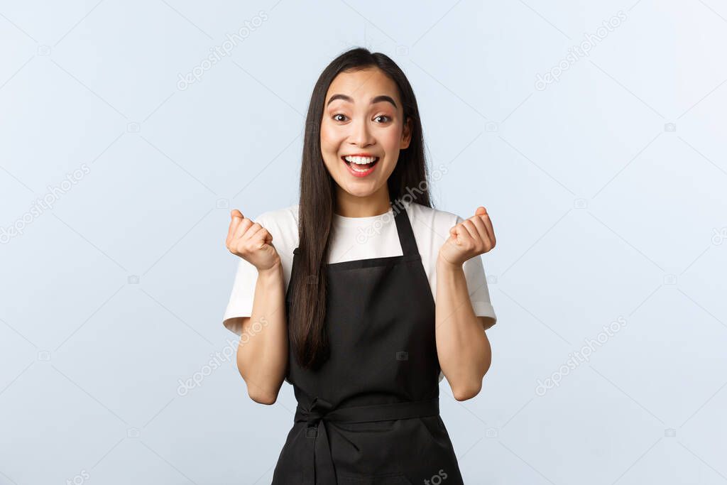 Coffee shop, small business and startup concept. Cheerful asian girl winning, best employee month, fist pump and rejoicing. Happy barista jumping enthusiastic, winning competition