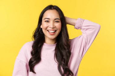 People emotions, lifestyle leisure and beauty concept. Close-up of friendly outgoing cute asian girl laughing and scratch back of head shy, receive praises for good job, stand yellow background clipart