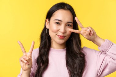 İnsanların duyguları, yaşam tarzı, eğlence ve güzellik konsepti. Kawaii güzel Japon kız barış işaretleri gösteriyor ve sevimli gülümsüyor, sarı arka plan reklam ürünlerinin başında duruyor.