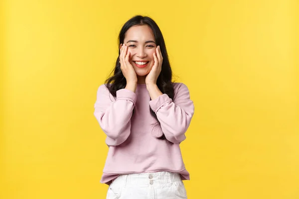 Les gens émotions, style de vie et concept de mode. Adorable fille coréenne souriante regardant heureux, se réjouissant de grandes nouvelles étonnantes, tenir la main sur le visage et debout fond jaune optimiste — Photo