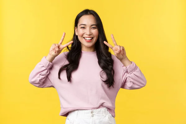 As pessoas emoções, estilo de vida e conceito de moda. alegre kawaii ásia menina no elegante roupa mostrando paz sinal e sorrindo otimista com branco dentes, pé sobre amarelo fundo, desfrutar de verão — Fotografia de Stock