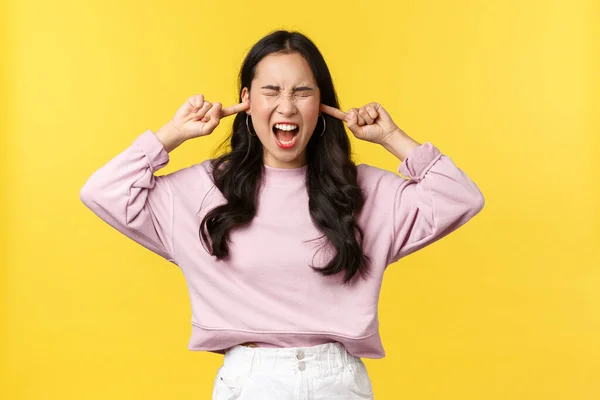 Gente emociones, estilo de vida y concepto de moda. Mujer asiática joven angustiada y loca gritando con los ojos cerrados y la cara indignada, oídos cerrados, sin ganas de escuchar, fondo amarillo — Foto de Stock