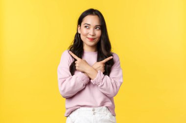 İnsan duyguları, yaşam tarzı konsepti. Şık giyinmiş kendinden emin Asyalı kız solcu ve tatmin olmuş görünüyordu. Kararlıydı, parmaklarını yana çevirerek, sarı arka planda.