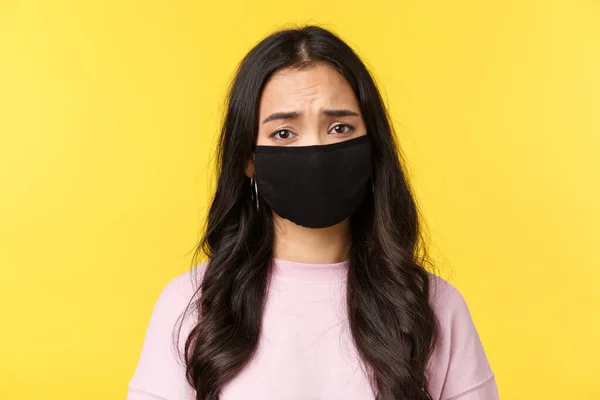 Covid-19, estilo de vida social-distanciamiento, prevenir el concepto de propagación del virus. Lástima y triste asiática sombría chica frunciendo el ceño, usar mascarilla, sentir compasión y tristeza, de pie fondo amarillo — Foto de Stock