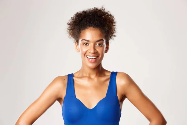 Närbild av attraktiv frisk kvinna i blå sport behå, ler mot kameran, står över vit bakgrund — Stockfoto