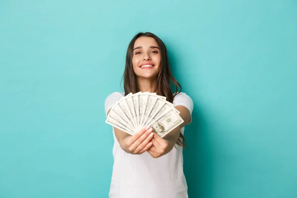 Retrato de mujer exitosa y feliz, vistiendo camiseta blanca, dándole dinero y sonriendo, de pie sobre fondo azul — Foto de Stock