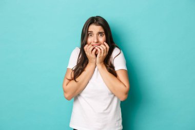 Beyaz tişörtlü, tırnak yiyen ve korkudan titreyen korkmuş güzel bir kız görüntüsü.