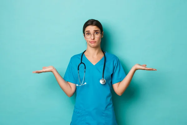 Coronavirus, πανδημία και κοινωνική έννοια αποστασιοποίησης. Εικόνα μιας ανίδεης γυναίκας γιατρού με ποτηράκια και ποτηράκια, με απλωμένα τα χέρια στο πλάι, να φαίνεται μπερδεμένη, να στέκεται πάνω από το μπλε φόντο — Φωτογραφία Αρχείου