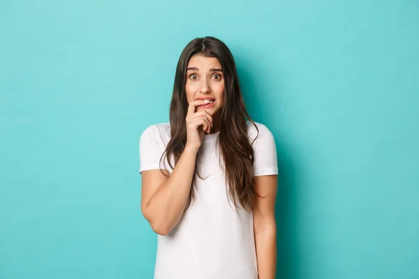 Immagine di insicura ragazza carina cercando preoccupato e indeciso, paura di qualcosa, mordere il dito e guardando insicuro, in piedi su sfondo blu — Foto Stock