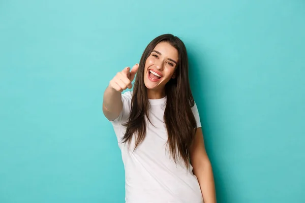 Χαρούμενη ελκυστική γυναίκα με λευκό t-shirt σας χρειάζονται, δείχνοντας κάμερα και χαμογελώντας, συγχαίροντας ή επιλέγοντας κάποιον, στέκεται πάνω από το μπλε φόντο — Φωτογραφία Αρχείου