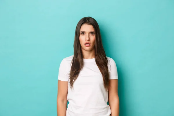 Immagine di ragazza bruna spaventata in t-shirt bianca, mascella goccia e guardando in soggezione, in piedi senza parole su sfondo blu — Foto Stock