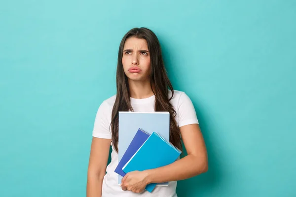 Kép a zaklatott és zaklatott női diák sóhajtozik, felnéz bosszús, gazdaság notebook, áll a kék háttér felett — Stock Fotó