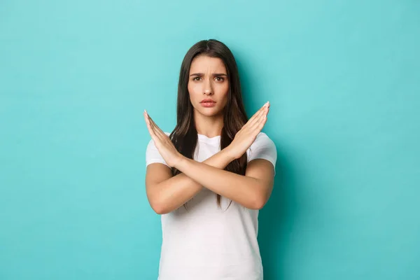 Donna preoccupata in t-shirt bianca proibire qualcosa di male, mostrando gesto trasversale e accigliato dispiaciuto, dire di fermarsi, in piedi su sfondo blu — Foto Stock