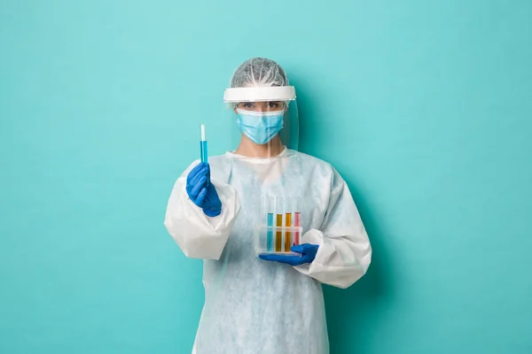 공감대 -19 의 개념 전염병과 건강. 자신있는 여성 기술 연구실 직원, 개인 보호 장비를 착용하고 시험관을 들고 백신을 보여 주며 푸른 배경에 만족 해 하는 모습 — 스톡 사진