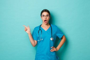 Coronavirus, salgın hastalık ve sosyalleşme konsepti. Güzel bayan doktorların yakından bakınca hayretler içinde, parmağını fotokopi alanına uzatmış, mavi arka planda dikiliyor.