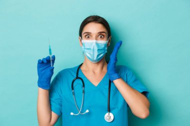 Covid-19 ve karantina kavramı. Tıbbi maskeli, eldivenli, önlüklü, elinde Coronavirus aşısı şırıngası tutan şaşırmış hemşire.