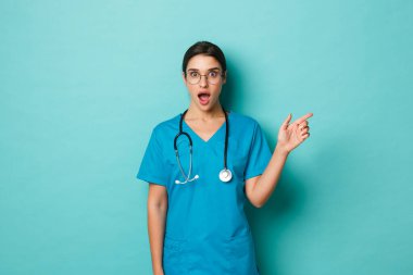 Coronavirus, salgın hastalık ve sosyalleşme konsepti. Gözlüklü ve önlüklü harika bir kadın doktor. Parmağıyla fotokopi alanını işaret ediyor. Şaşkın şaşkın bakıyor.