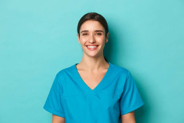 Coronavirus, sosyal uzaklık ve sağlık konsepti. Gülümseyen, önlük giyen, neşeli görünen, mavi arka planda duran genç bayan doktorların yakın çekimi. — Stok fotoğraf