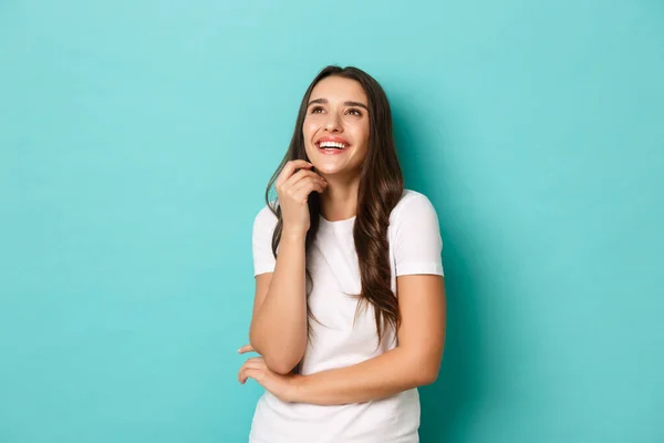 Imagem da bela mulher feliz com longo penteado escuro, vestindo t-shirt, rindo e olhando para o logotipo, de pé sobre fundo branco — Fotografia de Stock