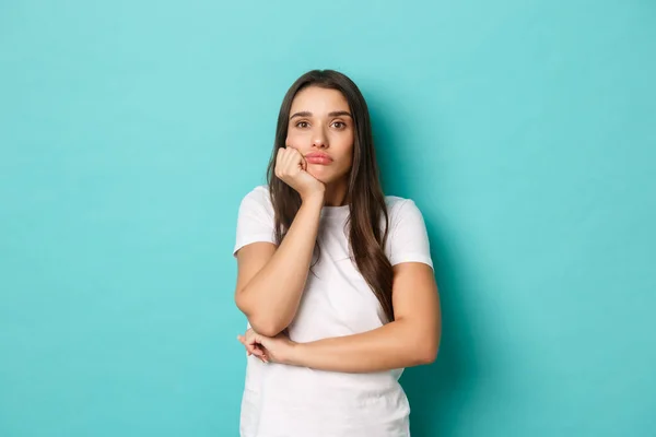 Droevige en sombere vrouw in wit t-shirt, bedachtzaam kijkend in de verte, staand over een blauwe achtergrond — Stockfoto