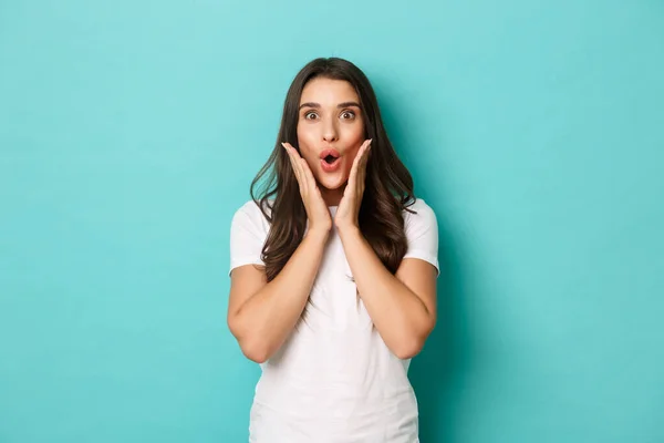 Image of surprised brunette girl reacting to announcement, gasping and looking at camera fascinated, gossiping over blue background — Stock Photo, Image