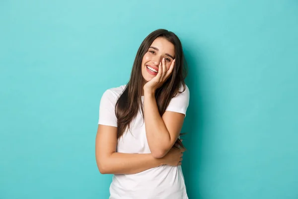 Imagem da mulher bonita feliz na t-shirt branca, rindo e tocando o rosto, de pé sobre o fundo azul — Fotografia de Stock