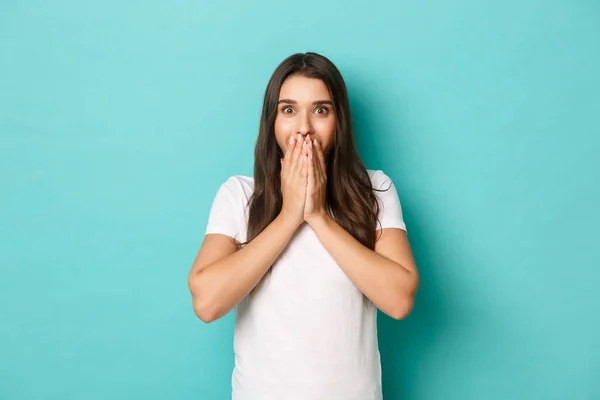 Portrait of surprised and excited brunette girl, looking amazed, cover mouth with hands, standing over blue background — Stock Photo, Image